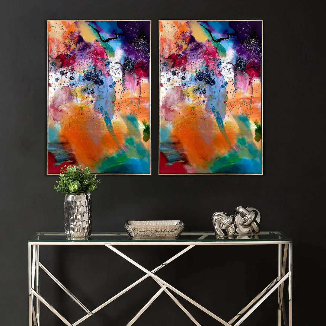 Two abstract paintings above a glass console table with decorative items.